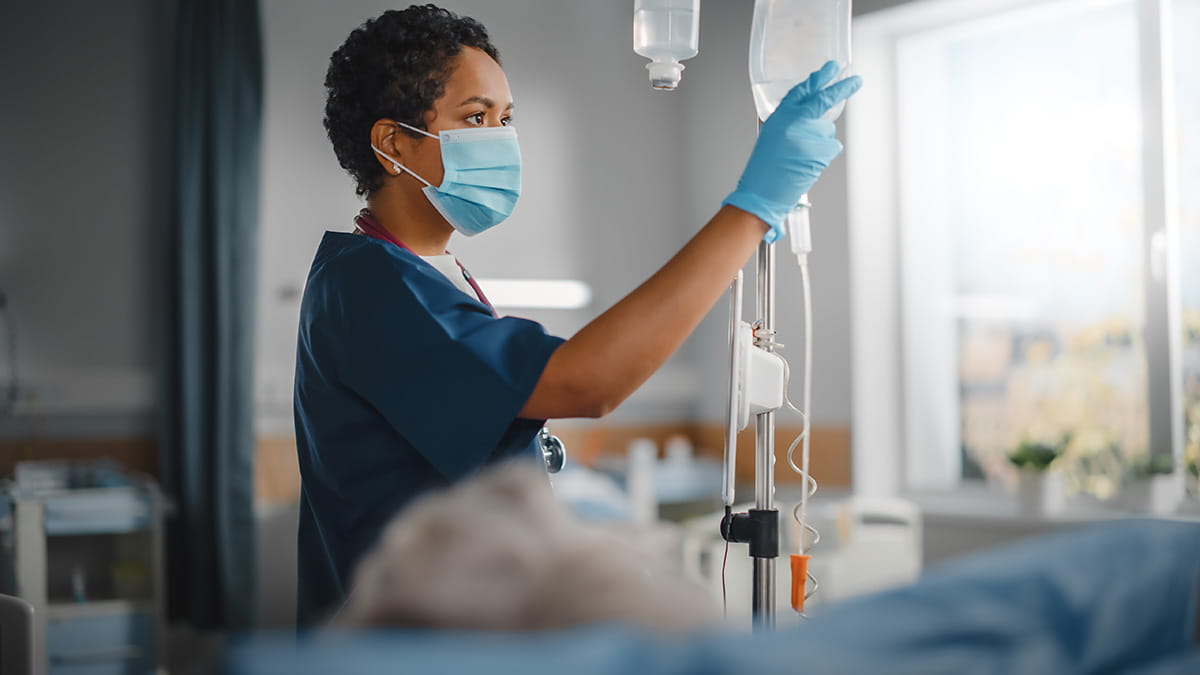 A cancer nurse in a hospital gown holds an IV drip, providing care and support to a patient in a clinical setting
